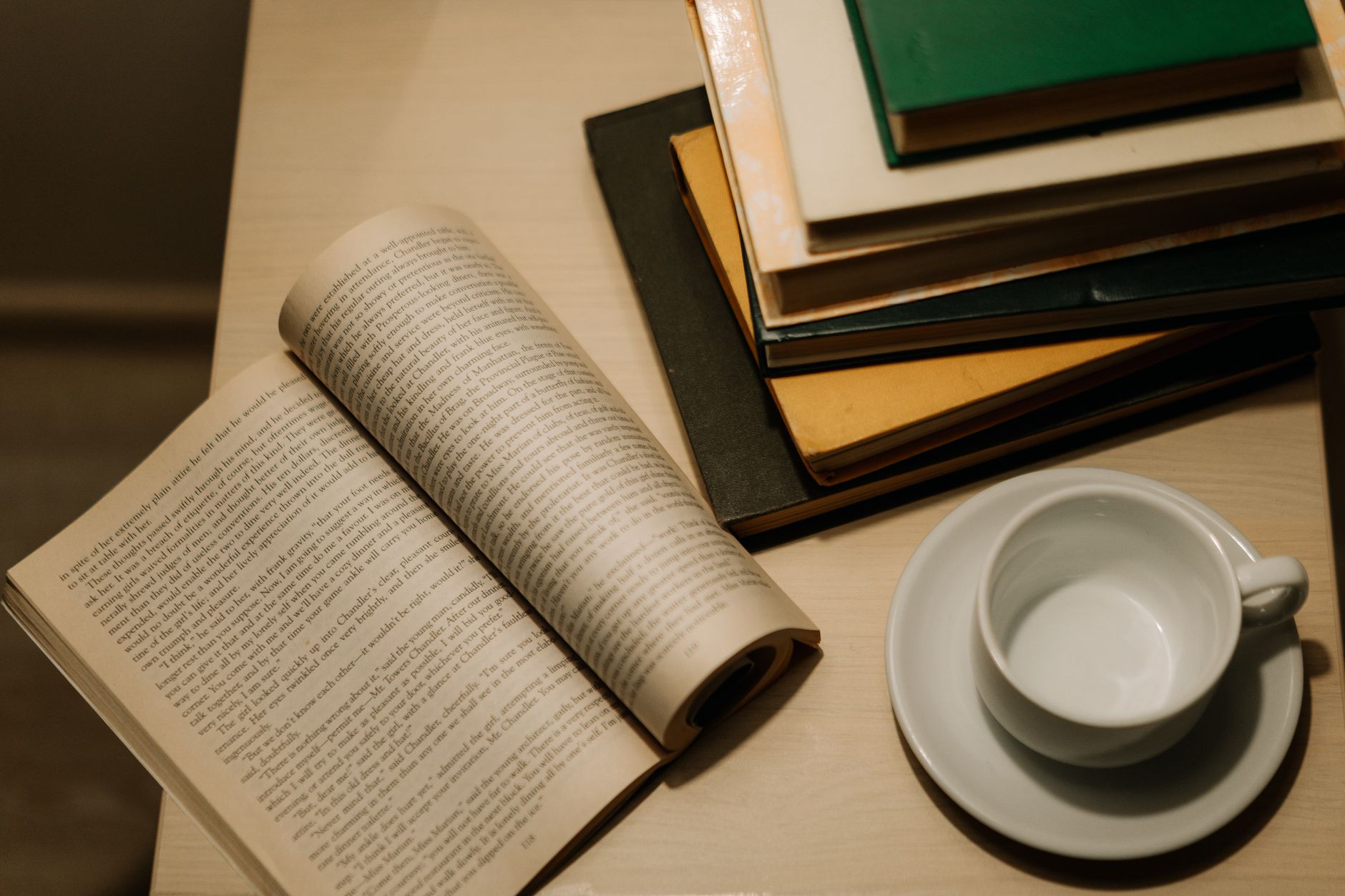 Livros empilhados e uma ch&aacute;vena numa mesa de madeira